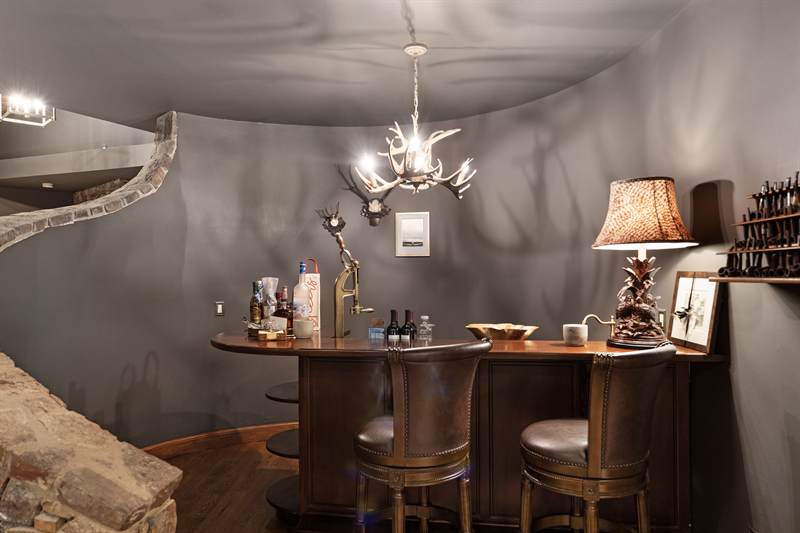 A small curved bar with leather stools beneath an antler chandelier