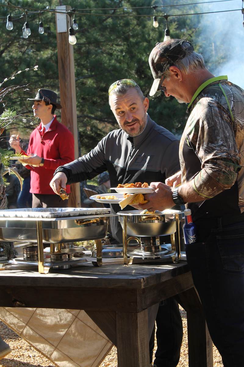 Guests serving themselves from chafing dishes on a long table under the pavilion